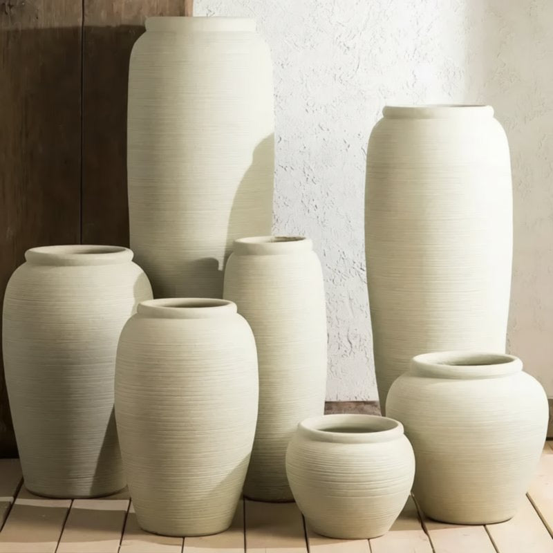 A collection of large, white, cylindrical vases arranged on a wooden floor against a white wall.