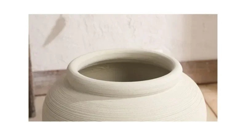 A white ceramic vase with a narrow neck and a wide base, sitting on a white surface against a plain background.