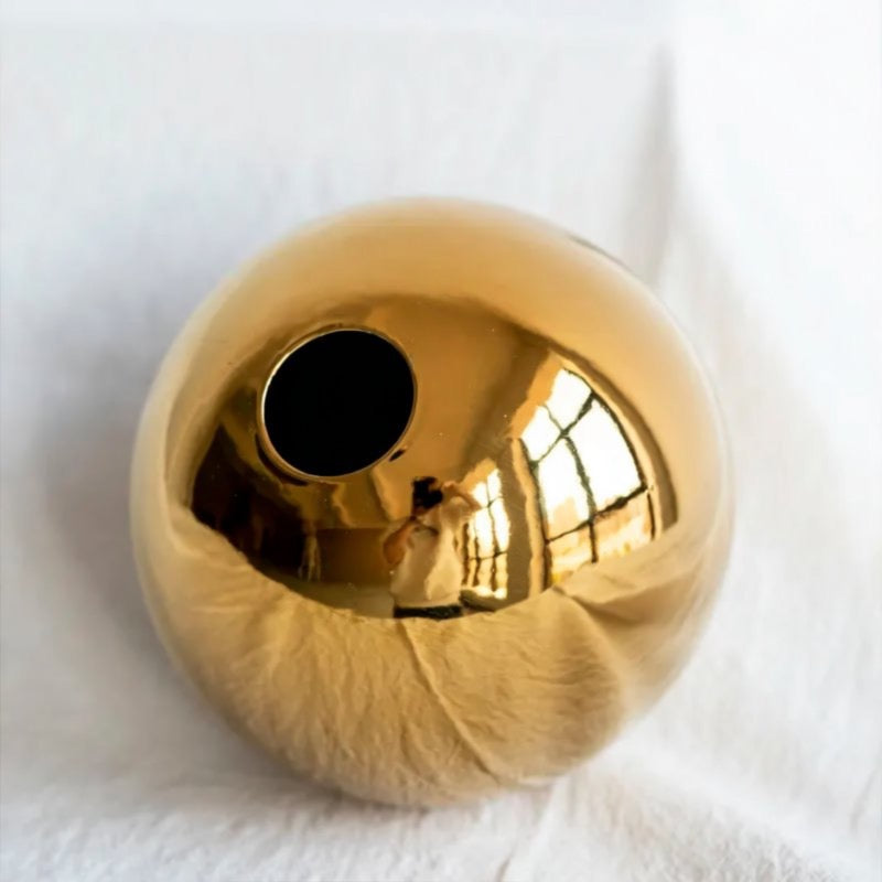 A shiny gold-colored sphere with a small hole in the center, reflecting the light and creating a mirror-like surface.